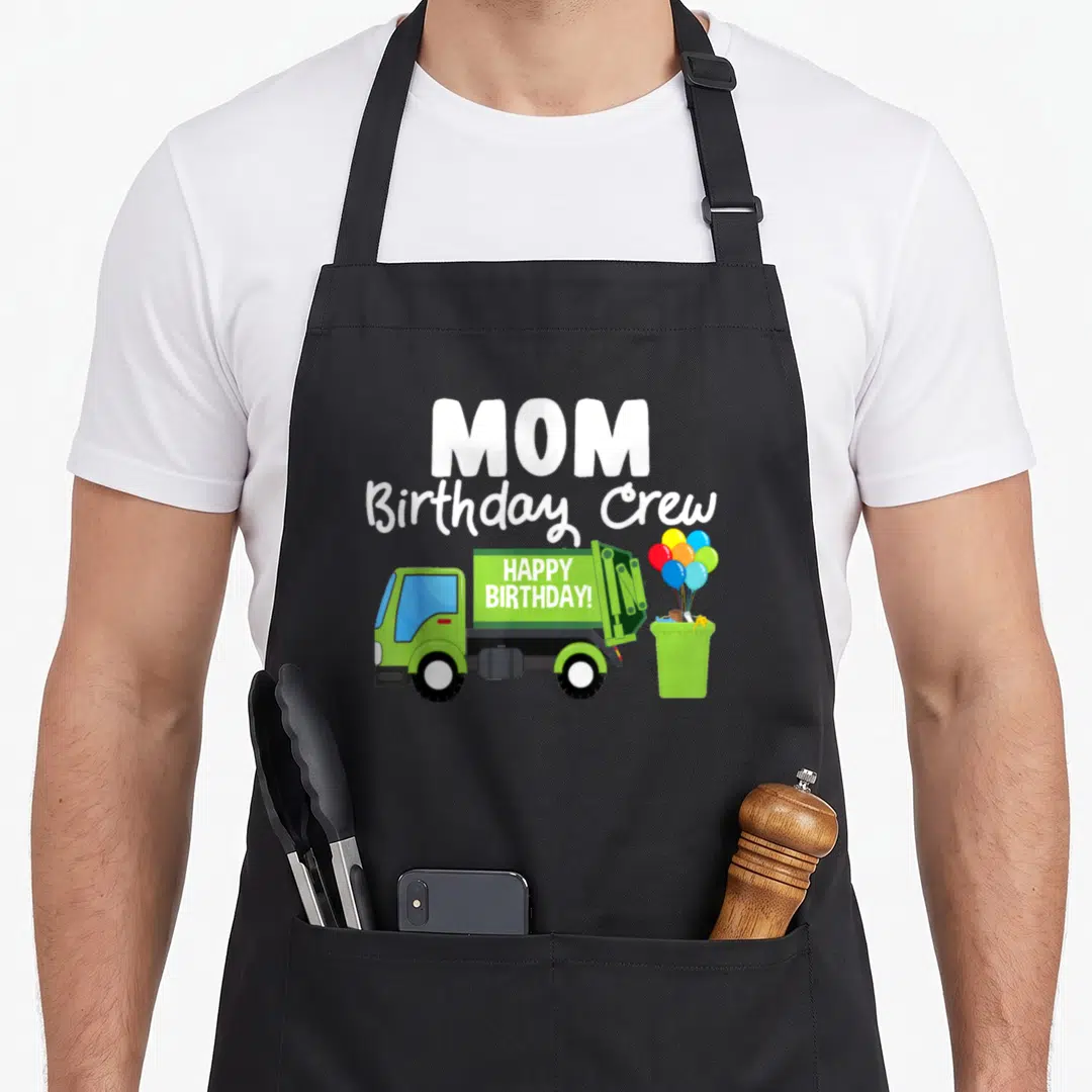 Garbage crew aprons - MOM Birthday Crew text above green truck with HAPPY BIRTHDAY! and balloons in bin — shown on a black cotton canvas apron against a white background