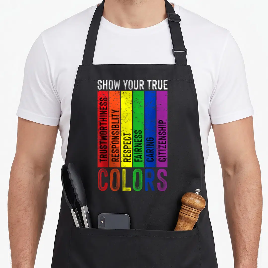 Lgtbq gay pride apron - Six vertical rainbow stripes with vertical virtue words and colorful COLORS text below — shown on a black cotton canvas apron against a white background