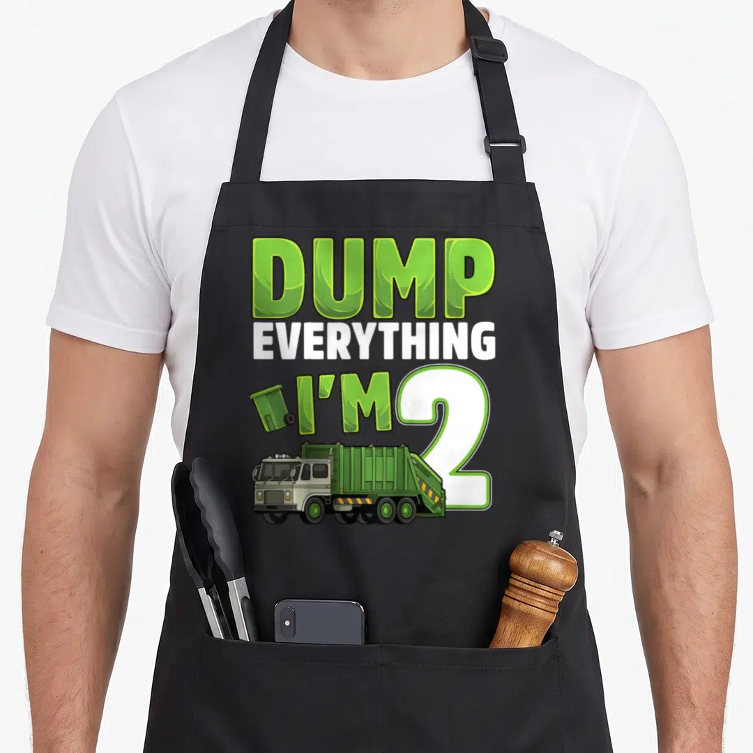 Garbage 2nd truck apron - DUMP EVERYTHING I'M 2 text with cartoon green garbage truck and trash can — shown on a black cotton canvas apron against a white background
