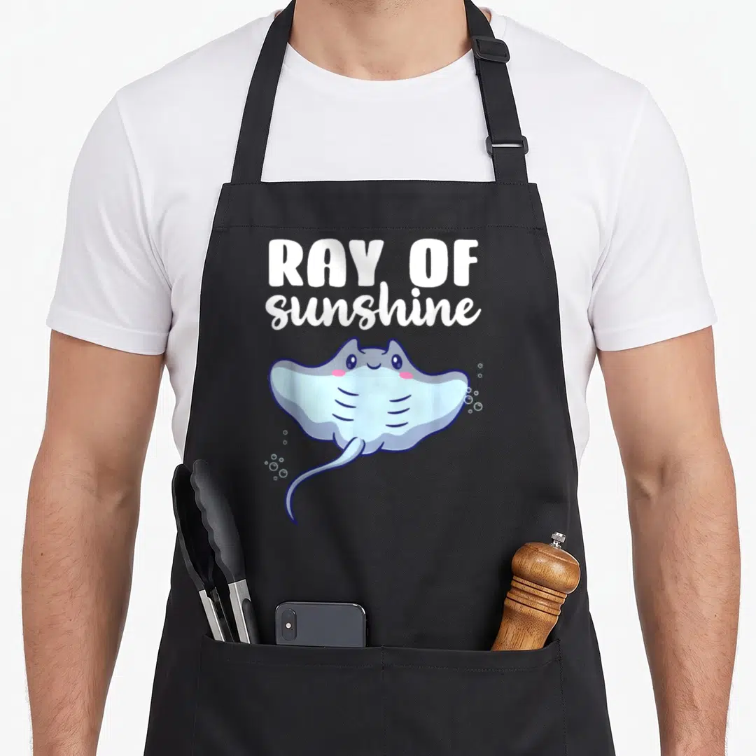 Ray kawaii apron - White ray of sunshine text above blue cartoon stingray with bubbles — shown on a black cotton canvas apron against a white background