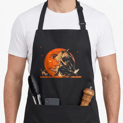 Moon halloween witch apron - Vintage line-art witch on crescent moon with broom and stars in orange and beige — shown on a black cotton canvas apron against a white background
