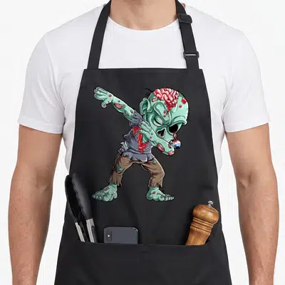 Zombie halloween apron - Cartoon zombie dabbing in green pink brown red with exposed brain and dangling eyeball — shown on a black cotton canvas apron against a white background