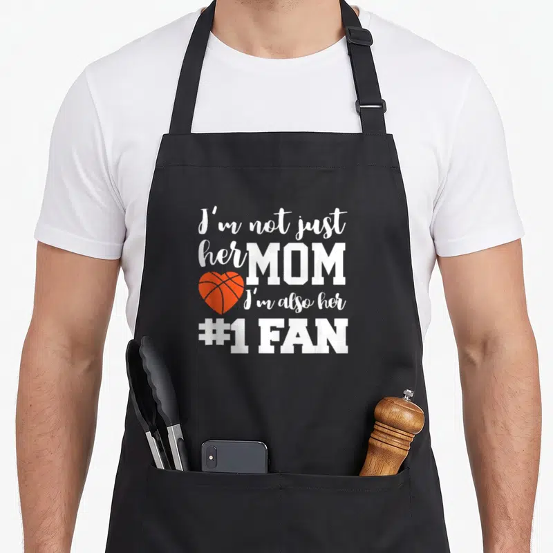 Basketball mother's apron - White text I'm not just her mom I'm also her number one fan next to orange heart basketball — shown on a black cotton canvas apron against a white background