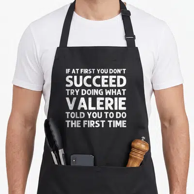 Valerie christmas apron - White text reading If At First You Don't Succeed Try Doing What Valerie Told You To Do — shown on a black cotton canvas apron against a white background