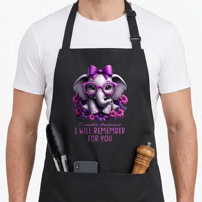 Elephant alzheimer's aprons - Cartoon grey elephant with purple bow glasses and flowers, text Dementia Awareness I Will — shown on a black cotton canvas apron against a white background
