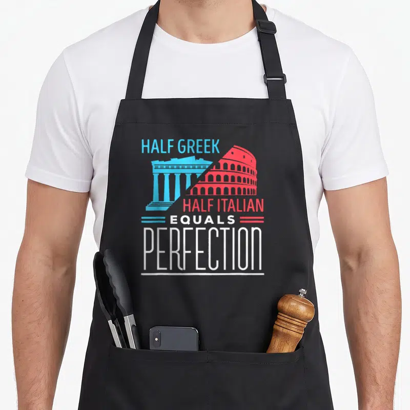 Greek italian apron - Blue Parthenon and red Colosseum merged diagonally with stacked text reading HALF GREEK HALF — shown on a black cotton canvas apron against a white background