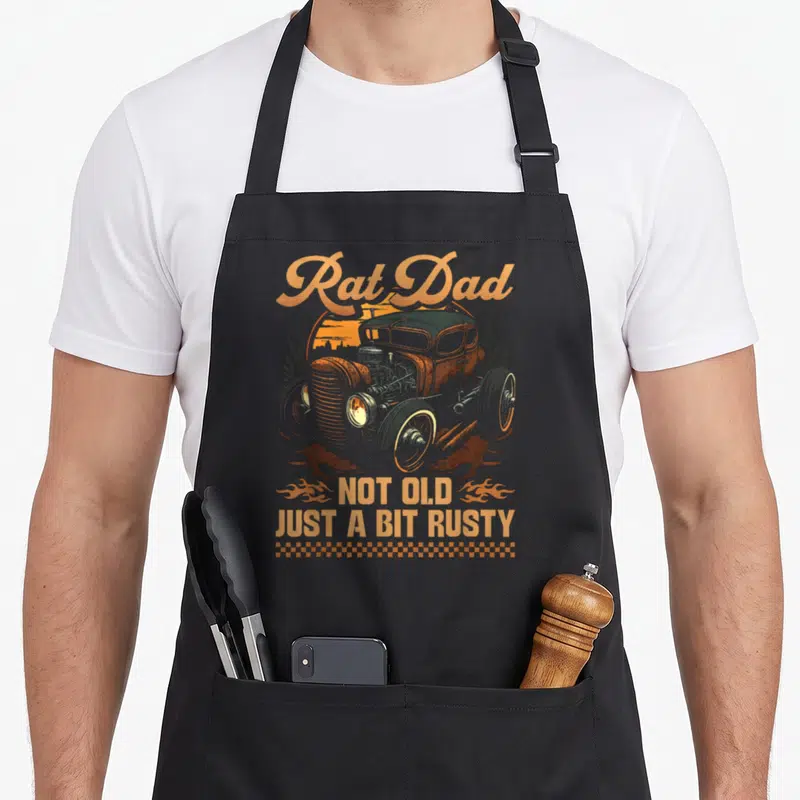 Hot rat dad apron - Retro hot rod car with arched Rat Dad text and rusty quote flanked by flames — shown on a black cotton canvas apron against a white background