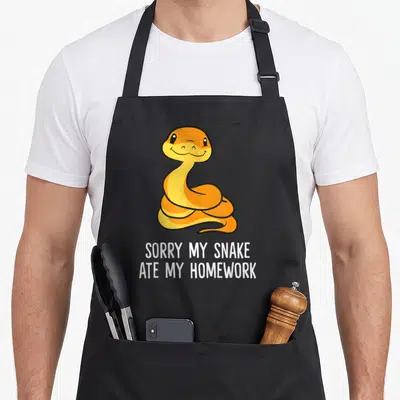 Snake pet apron - Orange coiled cartoon snake above white text reading sorry my snake ate my homework — shown on a black cotton canvas apron against a white background