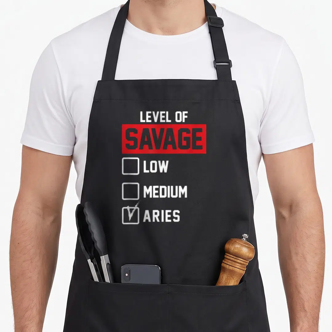 Level aries kitchen apron - Checklist graphic with Level of Savage text, red box, and checked Aries option in white — shown on a black cotton canvas apron against a white background