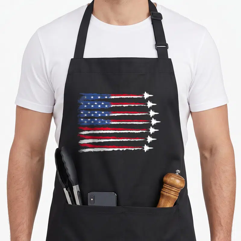 Blue patriotic apron - Eight white fighter jets flying right, contrails form distressed red white blue flag with stars — shown on a black cotton canvas apron against a white background