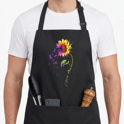 Fibromyalgia sunflower apron - Watercolor sunflower with purple ribbons and curved Fibro Awareness text — shown on a black cotton canvas apron against a white background