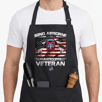 Flag paratrooper apron - 82nd Airborne text over USA flag with three parachutes and veteran dog tag in distressed red — shown on a black cotton canvas apron against a white background