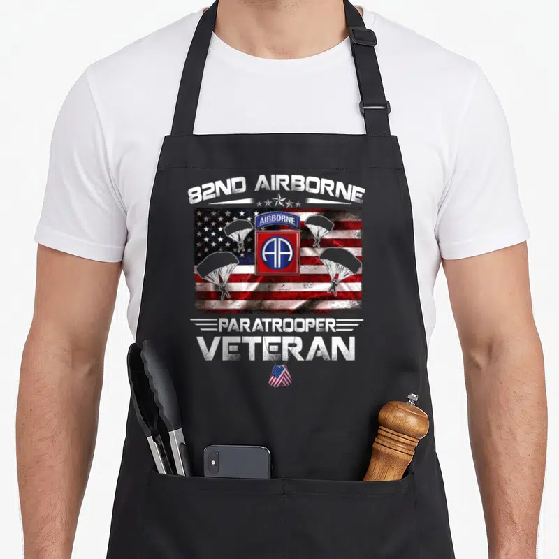Flag paratrooper apron - 82nd Airborne text over USA flag with three parachutes and veteran dog tag in distressed red — shown on a black cotton canvas apron against a white background