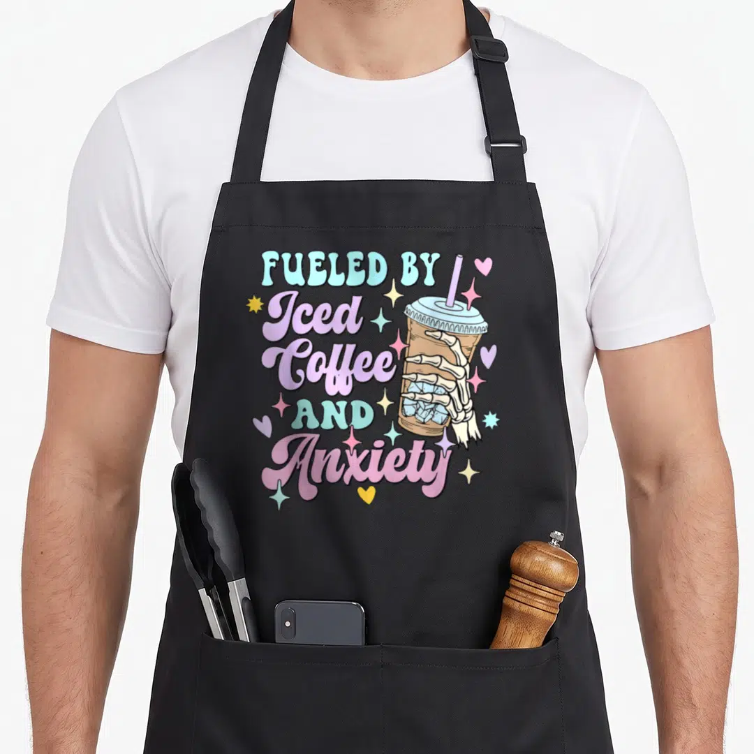 Iced coffee apron - Skeleton hand holding iced coffee cup with Fueled by Iced Coffee and Anxiety text in pastel colors — shown on a black cotton canvas apron against a white background