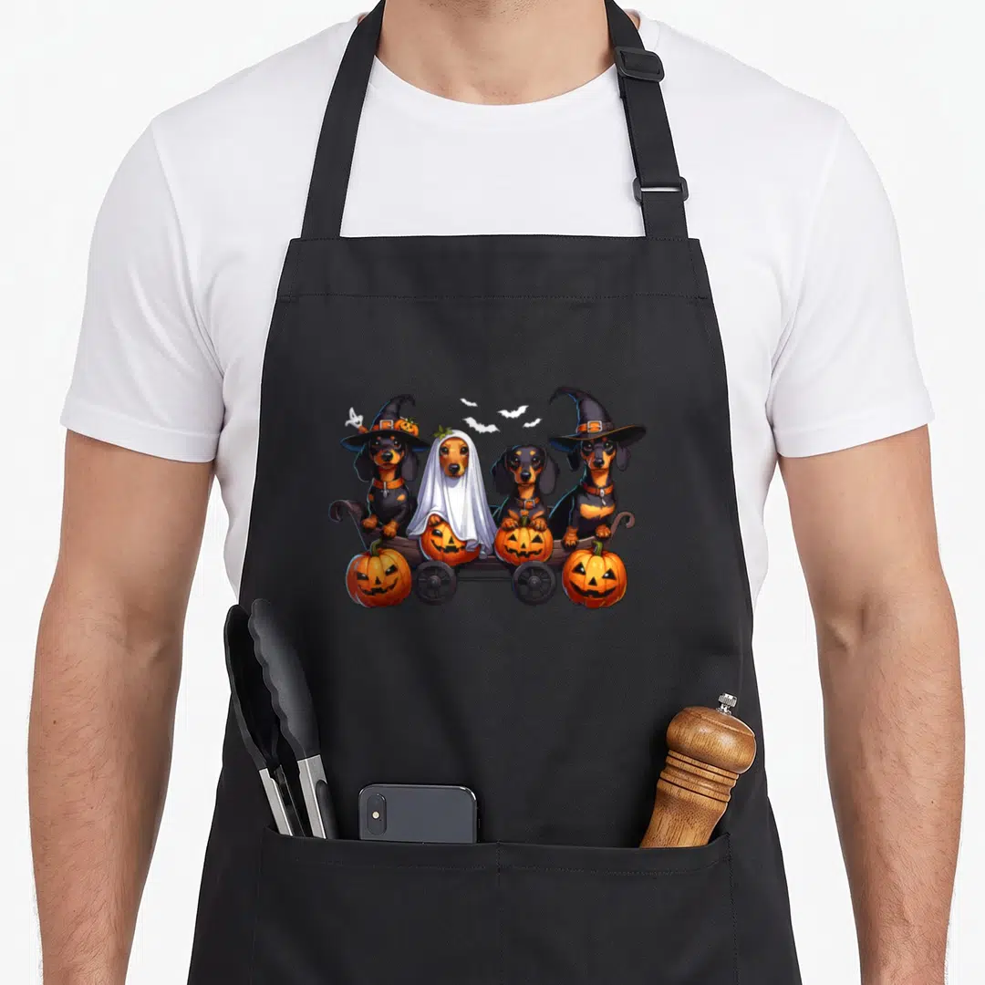 Dachshund cheap halloween aprons - Four dachshunds in Halloween costumes sitting in a wagon with pumpkins and flying — shown on a black cotton canvas apron against a white background