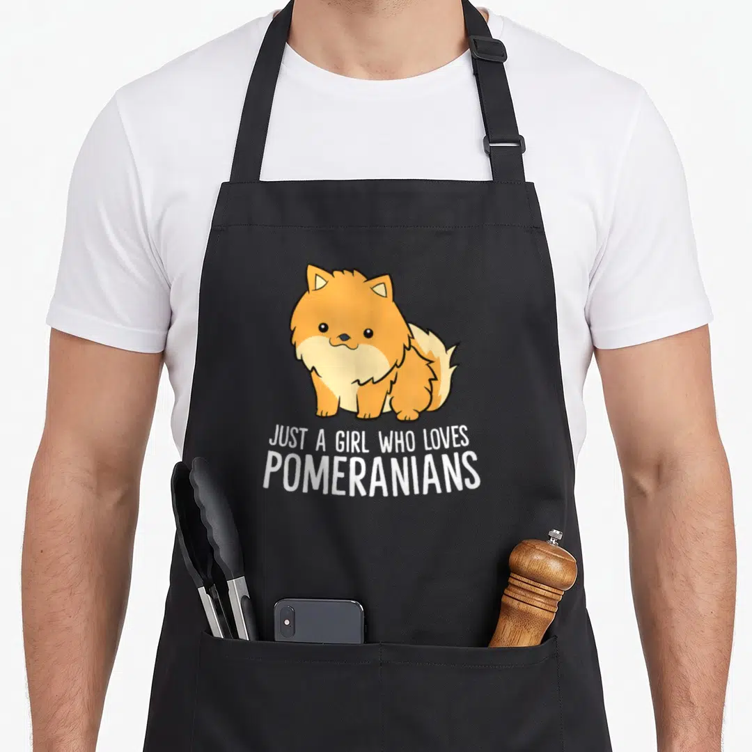 Pomeranian danish girl apron - Cartoon orange Pomeranian above white text JUST A GIRL WHO LOVES POMERANIANS — shown on a black cotton canvas apron against a white background