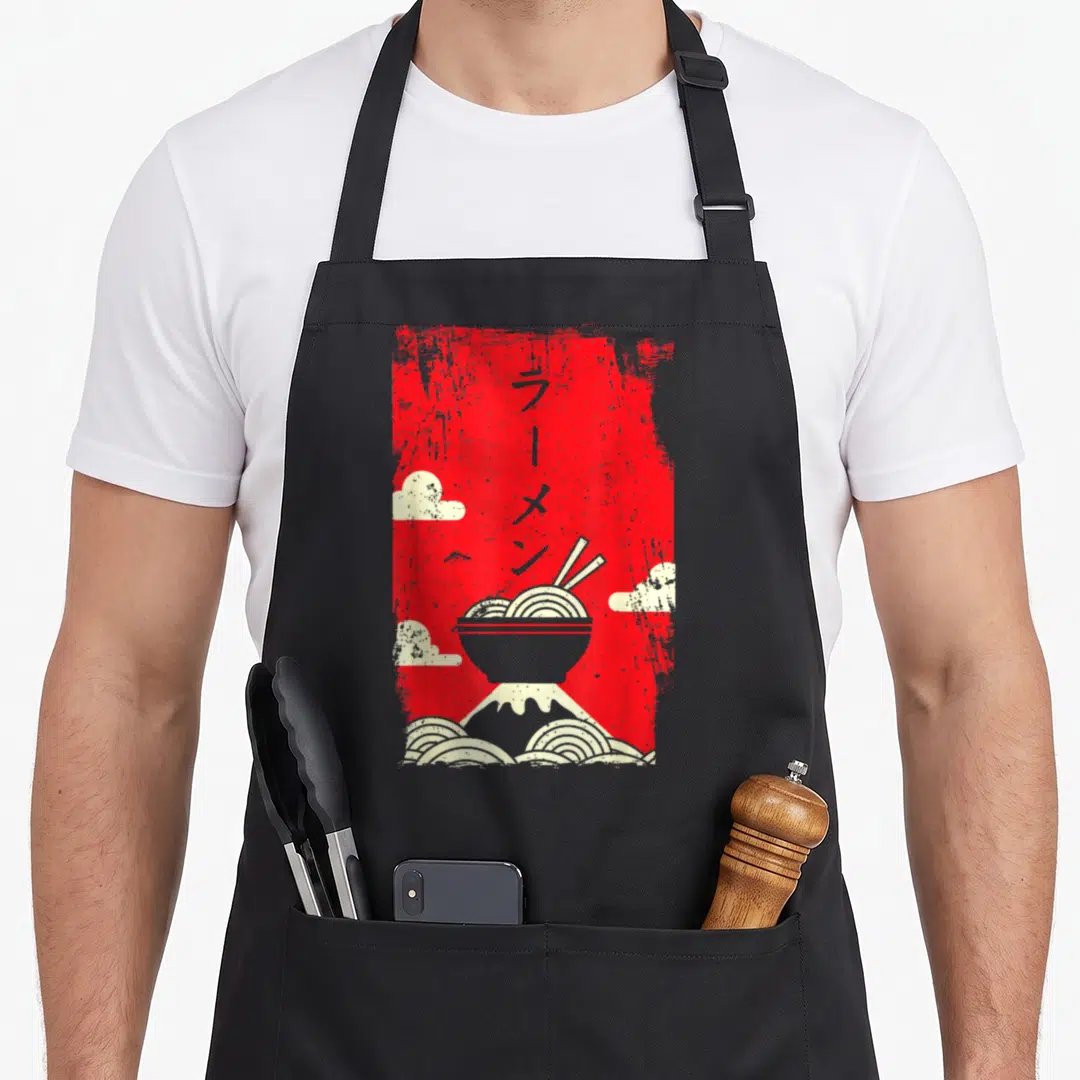 Japanese mein apron - Red distressed ramen bowl with vertical Japanese text, mountain, and clouds — shown on a black cotton canvas apron against a white background