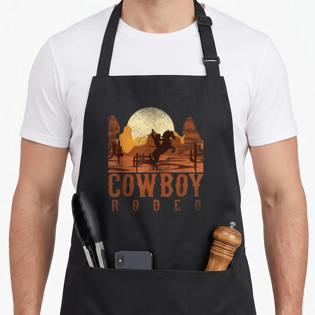 Rodeo texans apron - Retro cowboy riding bucking horse with COWBOY RODEO text in brown orange yellow — shown on a black cotton canvas apron against a white background