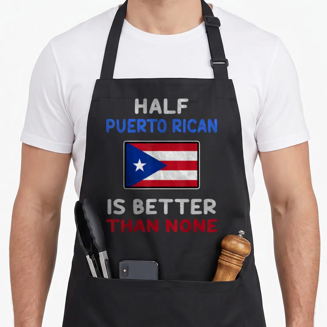 Puerto half birthday apron - Centered Puerto Rican flag with text HALF PUERTO RICAN IS BETTER THAN NONE in red, white — shown on a black cotton canvas apron against a white background