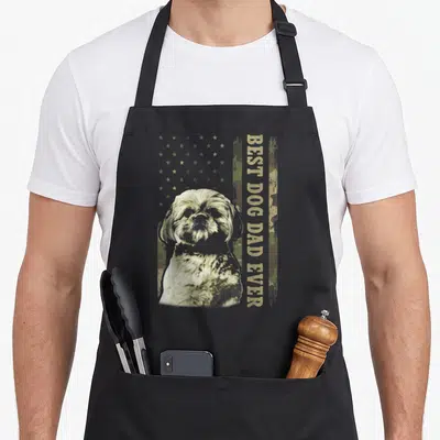 Shih camo apron - Realistic Shih Tzu head on tan green brown camo flag with vertical BEST DOG DAD EVER text — shown on a black cotton canvas apron against a white background