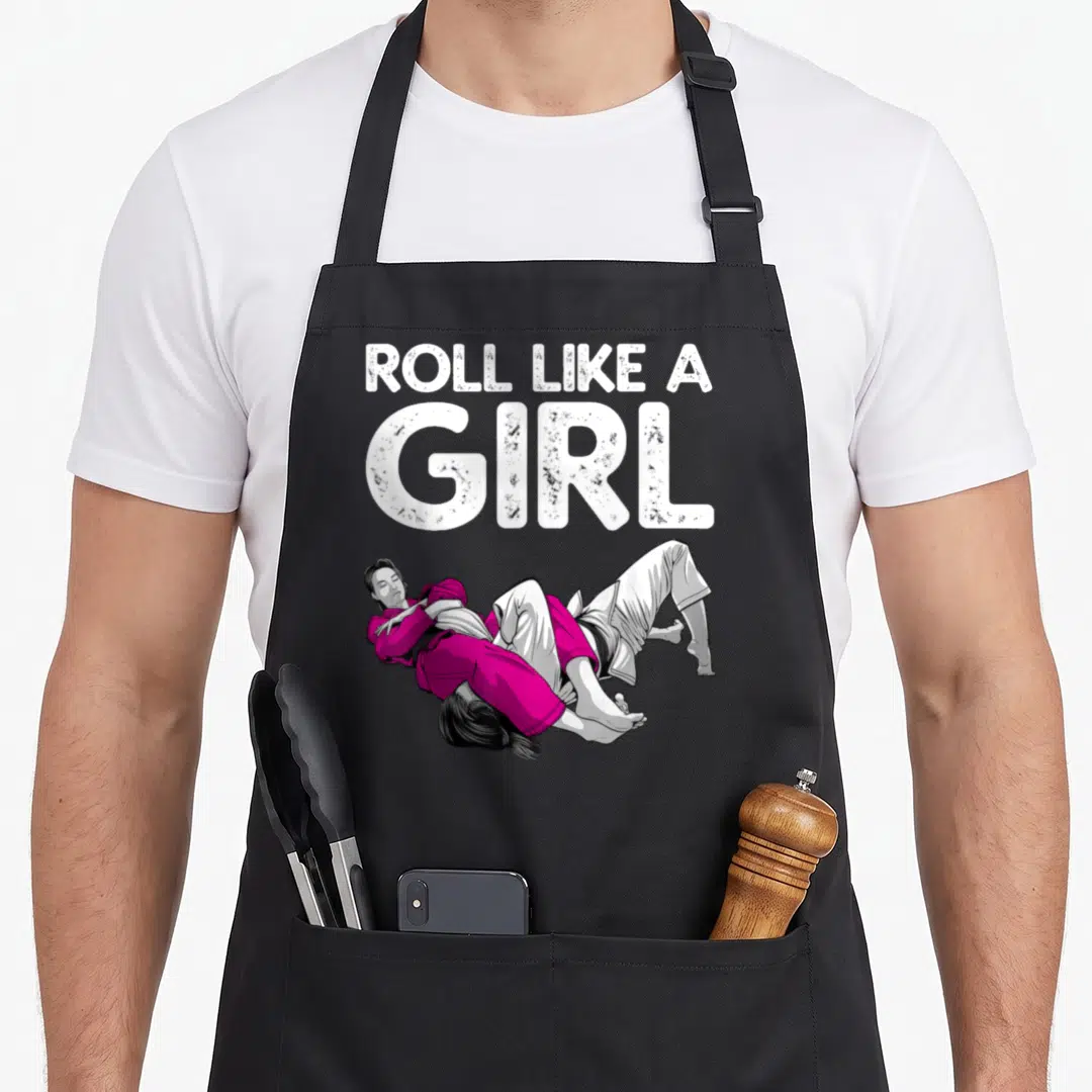 Jiu brazilian jitsu apron - Roll Like a Girl text above two cartoon grapplers in pink and black gis — shown on a black cotton canvas apron against a white background