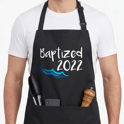 Baptized catholic apron - White Baptized 2022 text with blue water waves below — shown on a black cotton canvas apron against a white background