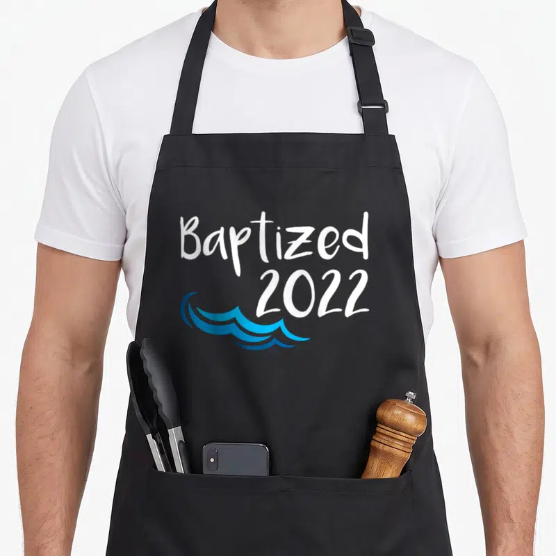 Baptized catholic apron - White Baptized 2022 text with blue water waves below — shown on a black cotton canvas apron against a white background
