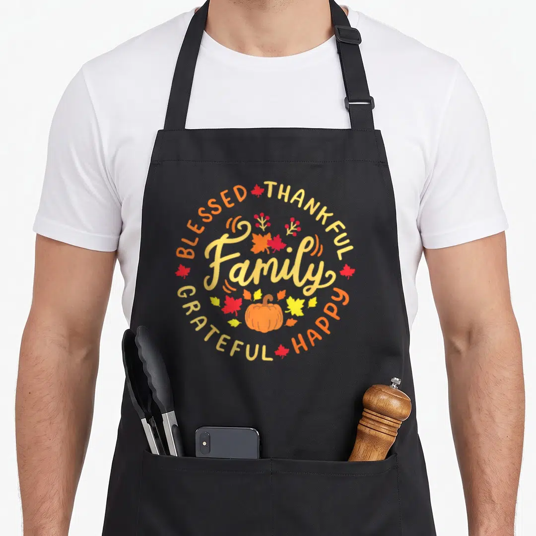 Blessed family thankful apron - Cartoon pumpkin and circular text BLESSED THANKFUL Family GRATEFUL HAPPY in autumn — shown on a black cotton canvas apron against a white background