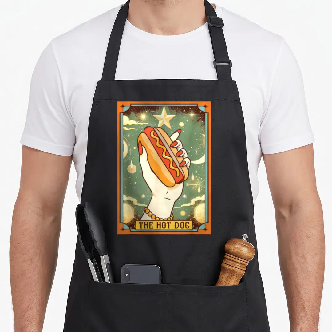 Bun hot dog apron - Retro tarot card style hand holding hot dog with mustard and THE HOT DOG text — shown on a black cotton canvas apron against a white background