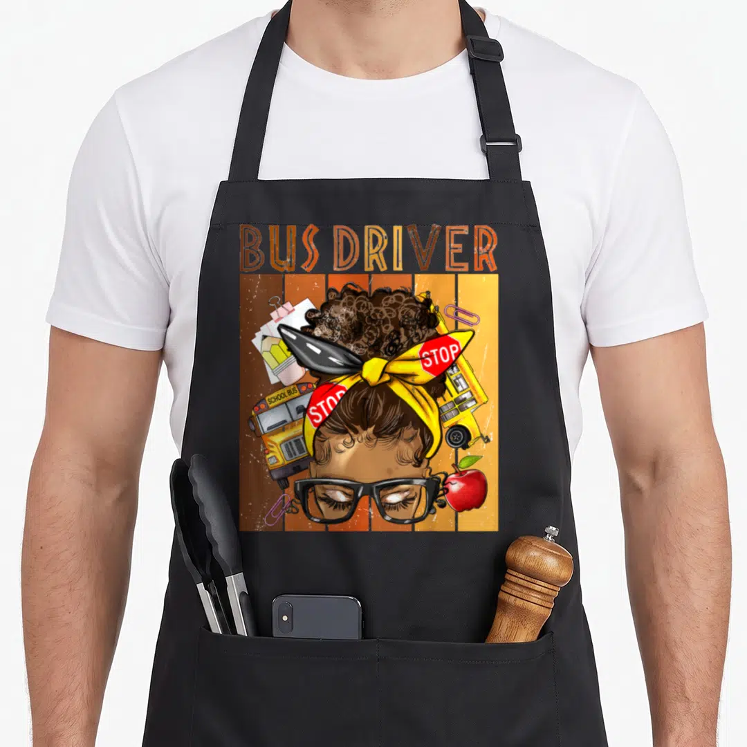 School messy aprons - BUS DRIVER text above woman with glasses, two buses, apple, and paper clips on striped background — shown on a black cotton canvas apron against a white background