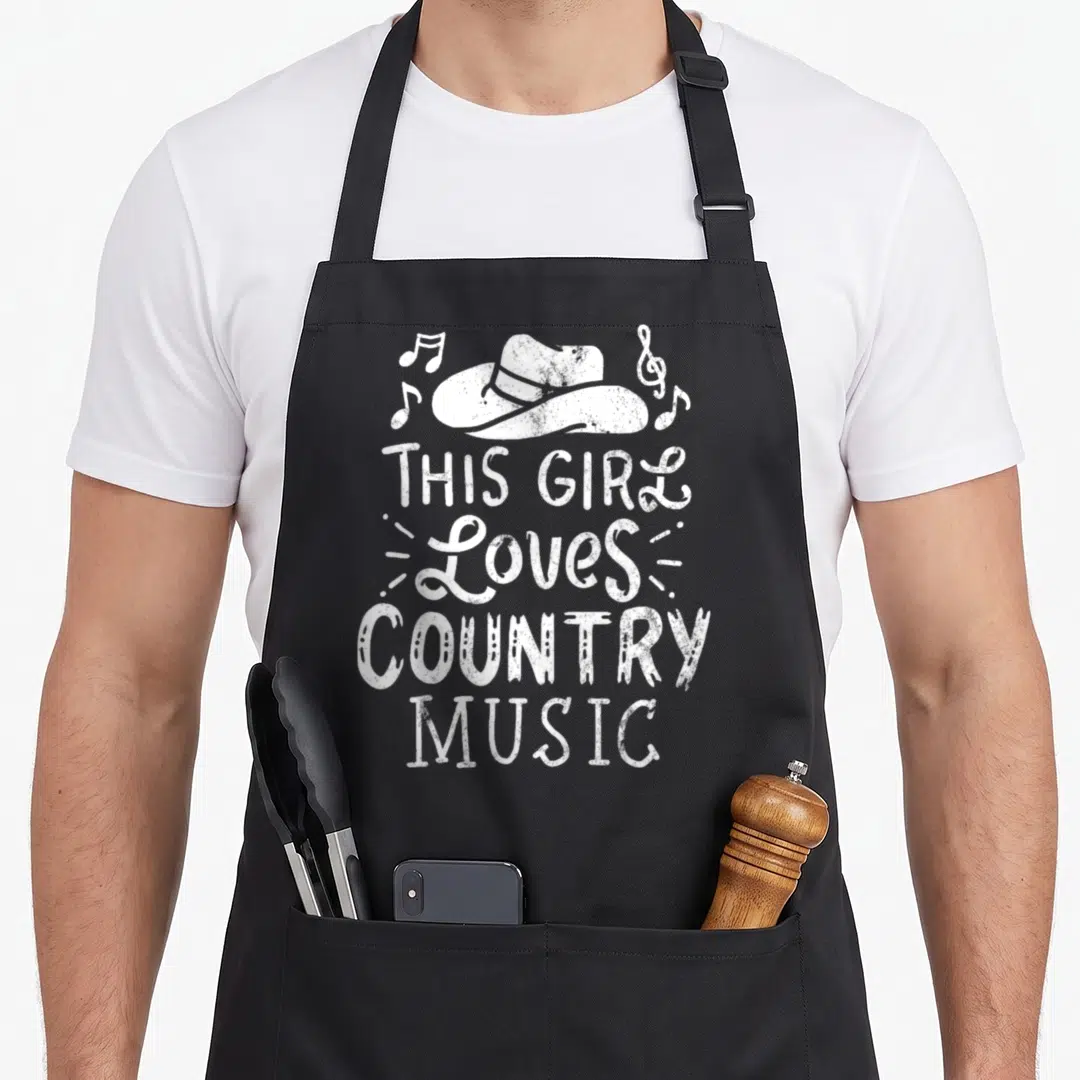 Western cook's country aprons - White cowboy hat and musical notes above stacked distressed text reading This Girl — shown on a black cotton canvas apron against a white background