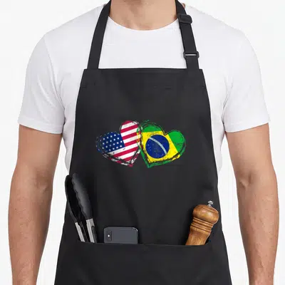 Funny brazil american flag apron - Two overlapping hearts with distressed US and Brazil flag colors — shown on a black cotton canvas apron against a white background