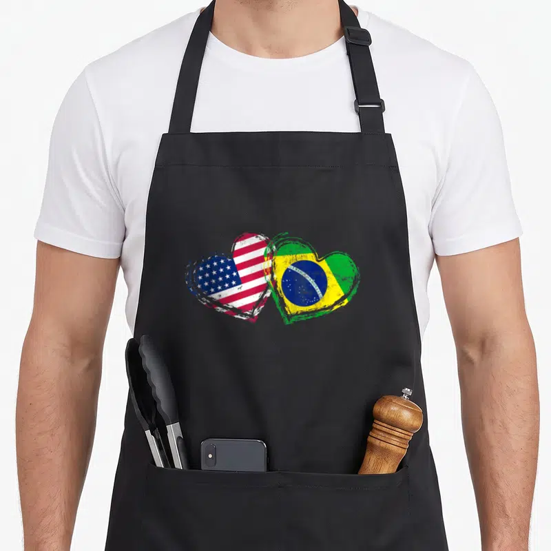 Funny brazil american flag apron - Two overlapping hearts with distressed US and Brazil flag colors — shown on a black cotton canvas apron against a white background