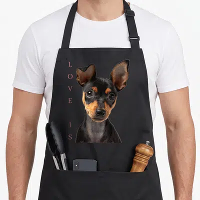 Miniature dog apron - Photo of black and tan dog head with vertical pink LOVES IS text to the left — shown on a black cotton canvas apron against a white background