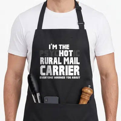 Psychotic birthday crew apron - Stacked white and dark grey text reading I'm The Psychotic Rural Mail Carrier Everyone — shown on a black cotton canvas apron against a white background