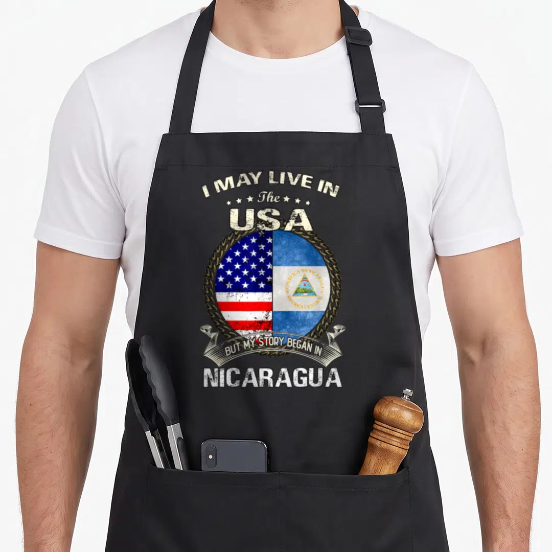 Nicaragua story of the apron - Split US and Nicaragua flags inside gold chain with distressed text — shown on a black cotton canvas apron against a white background