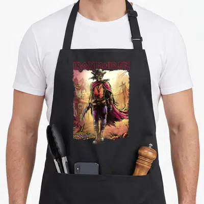 Mind novel apron - Skeleton cowboy standing before ruins with IRON MAIDEN text in red, purple, yellow, and orange — shown on a black cotton canvas apron against a white background
