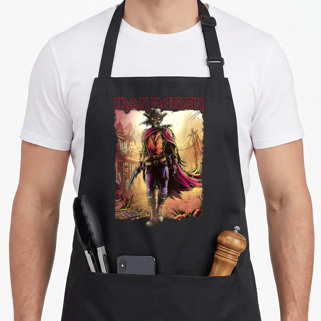 Mind novel apron - Skeleton cowboy standing before ruins with IRON MAIDEN text in red, purple, yellow, and orange — shown on a black cotton canvas apron against a white background