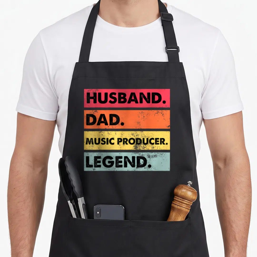 Husband making aprons - Stacked red orange yellow blue bars with black text Husband Dad Music Producer Legend distressed — shown on a black cotton canvas apron against a white background