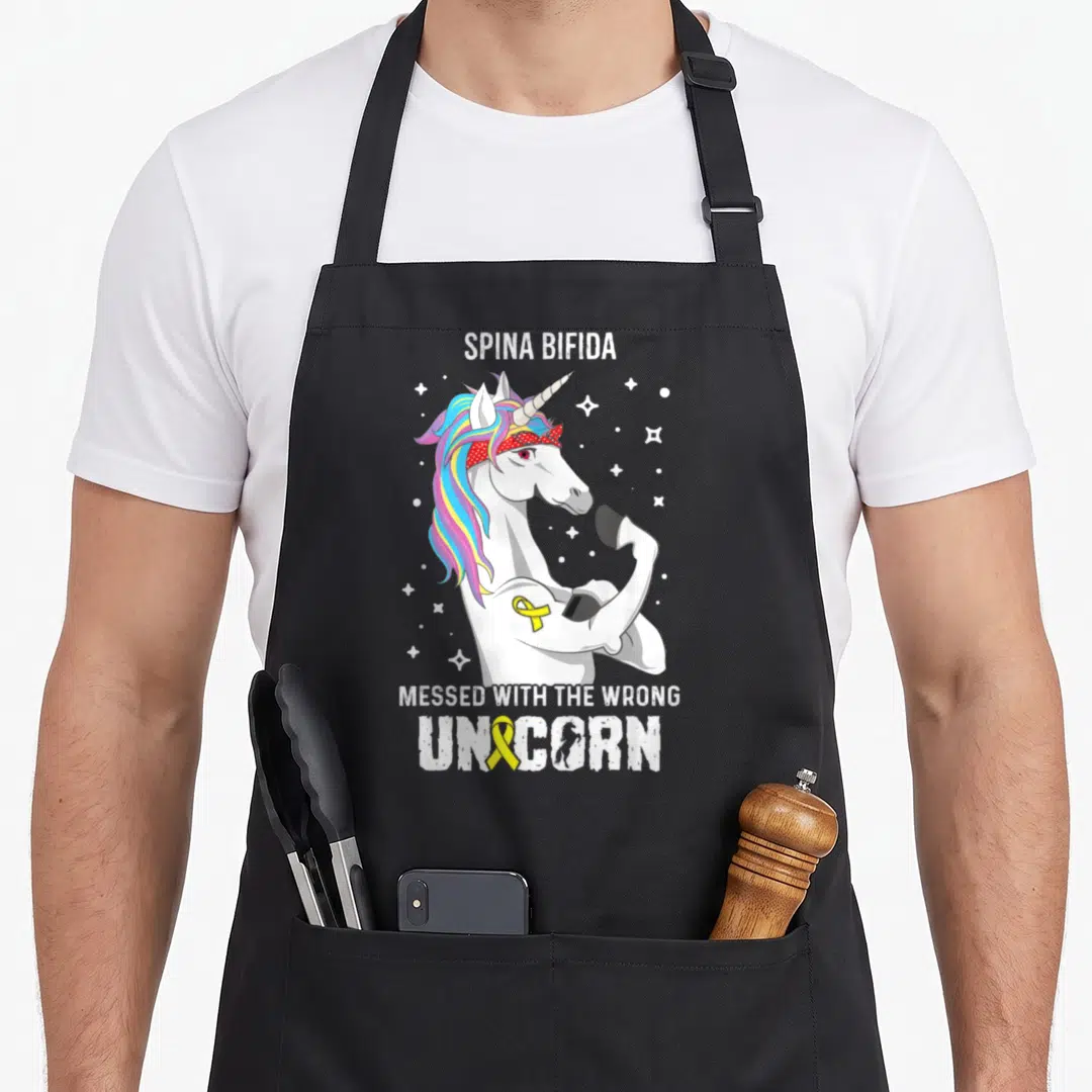 Wrong unicorn apron - Cartoon white unicorn with rainbow mane and yellow ribbon surrounded by stars and Spina Bifida — shown on a black cotton canvas apron against a white background
