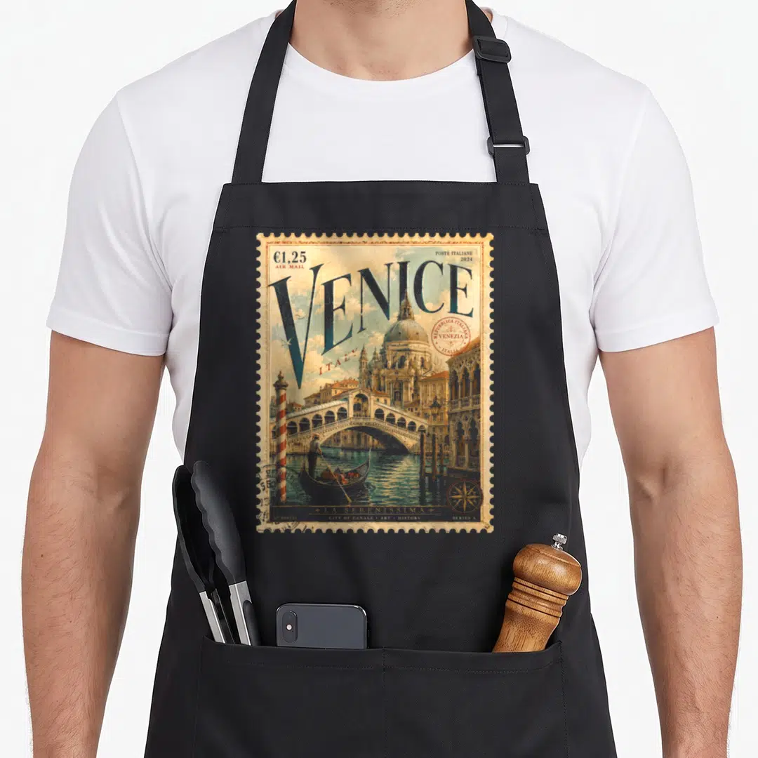 Postage italy apron - Retro Venice stamp design with blue VENICE text, red stamp, and gondola scene on tan background — shown on a black cotton canvas apron against a white background