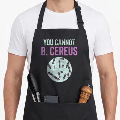 Microbiology teacher apron - YOU CANNOT B. CEREUS text above light blue circle with purple bacteria — shown on a black cotton canvas apron against a white background