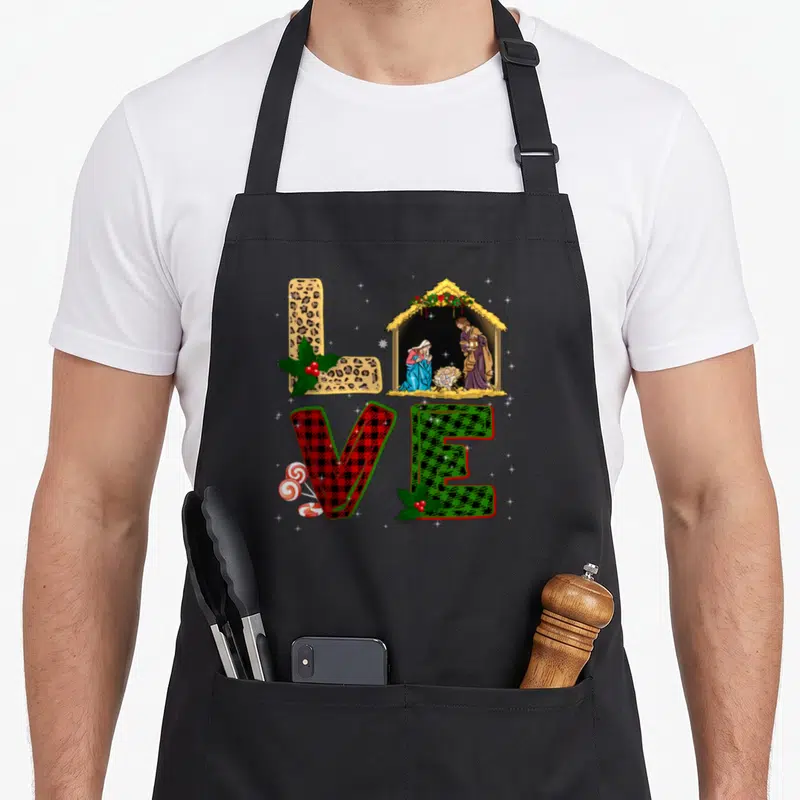 Leopard womens christmas apron - LOVE letters in leopard red and green plaid with nativity scene, holly, and peppermints — shown on a black cotton canvas apron against a white background