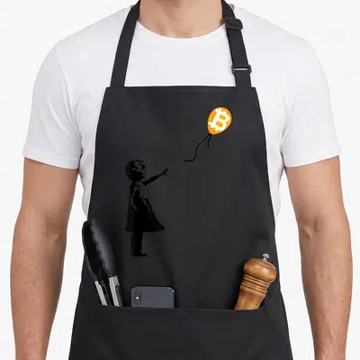 Btc balloon apron - Black child silhouette reaching for orange balloon with white Bitcoin logo inside — shown on a black cotton canvas apron against a white background