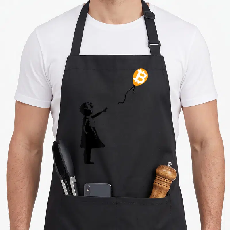 Btc balloon apron - Black child silhouette reaching for orange balloon with white Bitcoin logo inside — shown on a black cotton canvas apron against a white background
