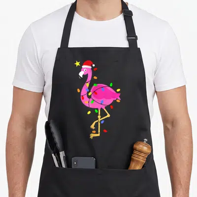 Hat pink flamingo apron - Pink flamingo wearing red Santa hat wrapped in multicolored Christmas lights with yellow star — shown on a black cotton canvas apron against a white background