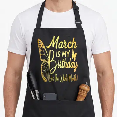 Vintage march birthday apron - Gold butterfly and text reading March IS MY Birthday Yes The Whole Month — shown on a black cotton canvas apron against a white background