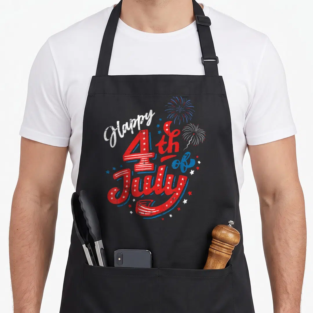 Cute independence 4th of july apron - Red white and blue Happy 4th of July text with two fireworks and scattered stars — shown on a black cotton canvas apron against a white background