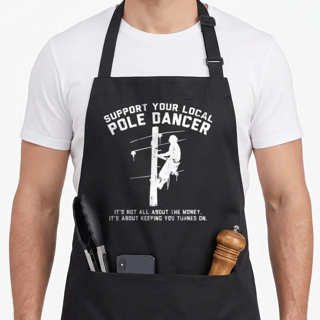Support electrician apron - White distressed lineman climbing pole with Support Your Local Pole Dancer text — shown on a black cotton canvas apron against a white background