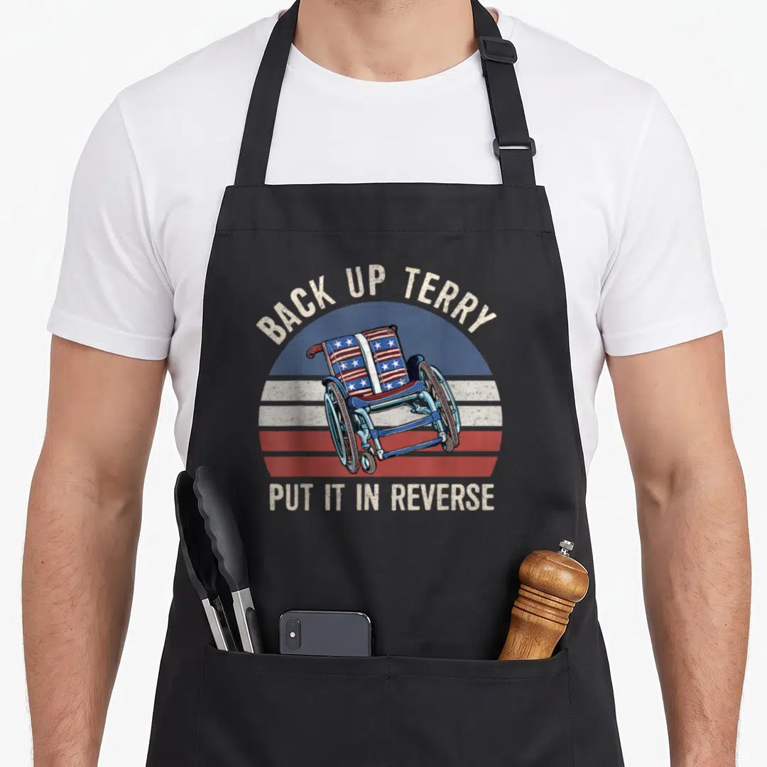 Reverse firework 4th of july apron - Wheelchair with flag pattern against striped sun and arched text reading BACK UP — shown on a black cotton canvas apron against a white background